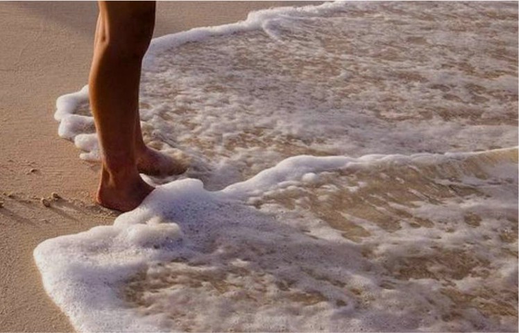 feet in the sand with the ocean washing over them