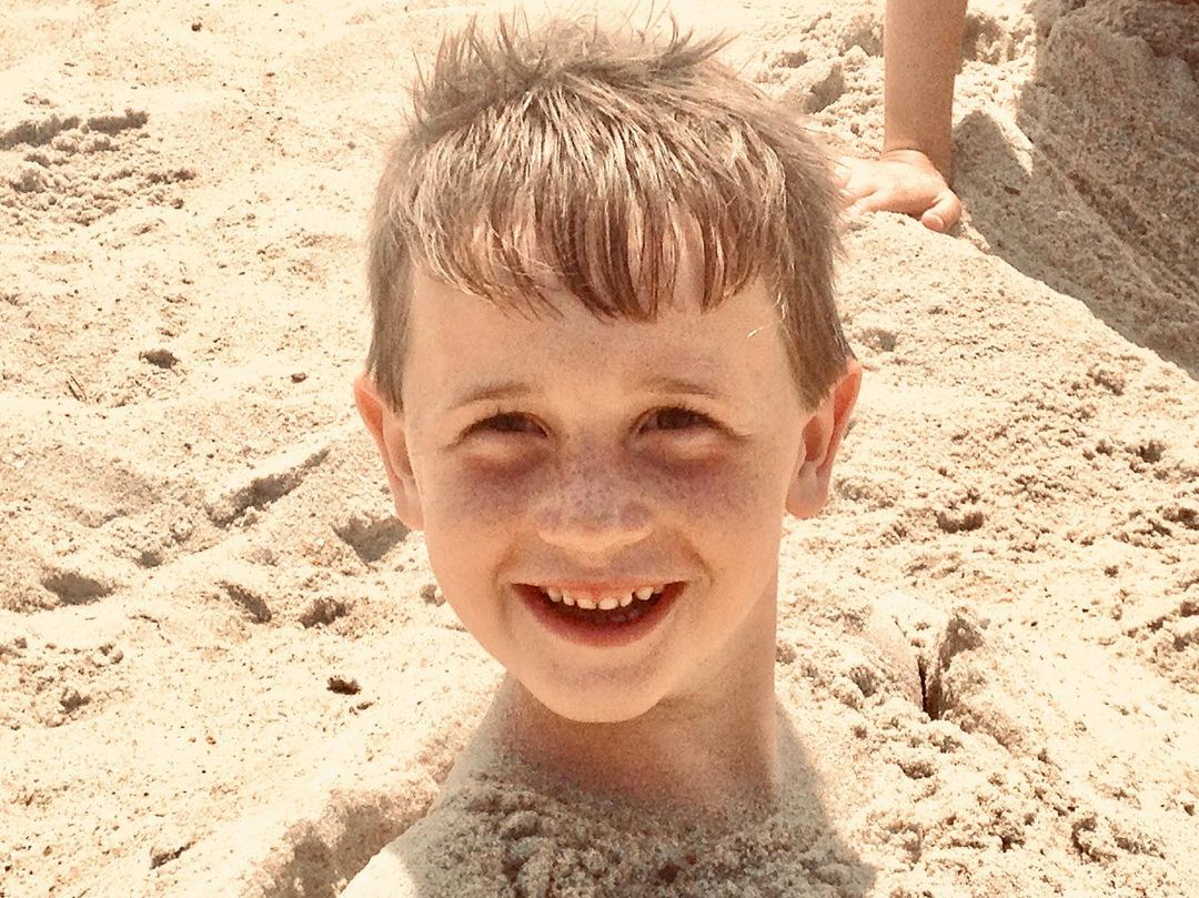 Young boy smiling with his hand sticking up out of the sand